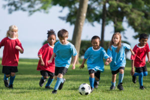 A multi-ethnic group of elementary age children are playing a soccer game outside on a sunny day at the park.