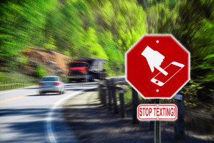 Stop sign with a symbol of a handheld device and the words Stop Texting printed on it. Image is blurred to imply motion and distraction. Symbol is artist own conceptual design.